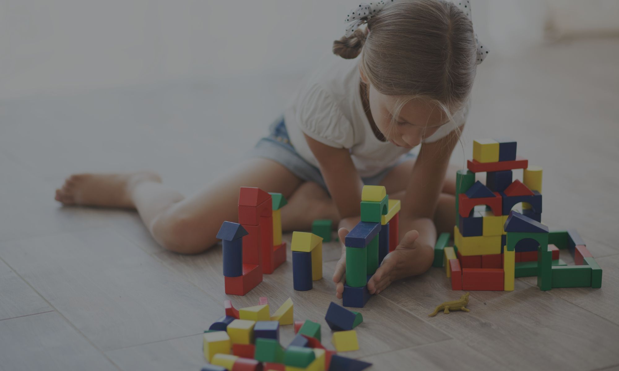 uma menina criança brincando sozinha, olhando para baixo, quietinha e concentrada. Ela se entretém na brincadeira com blocos de madeira de montar - está criando o próprio mundo. Comportamento típico de filhos com maior traço corporal esquizoide.