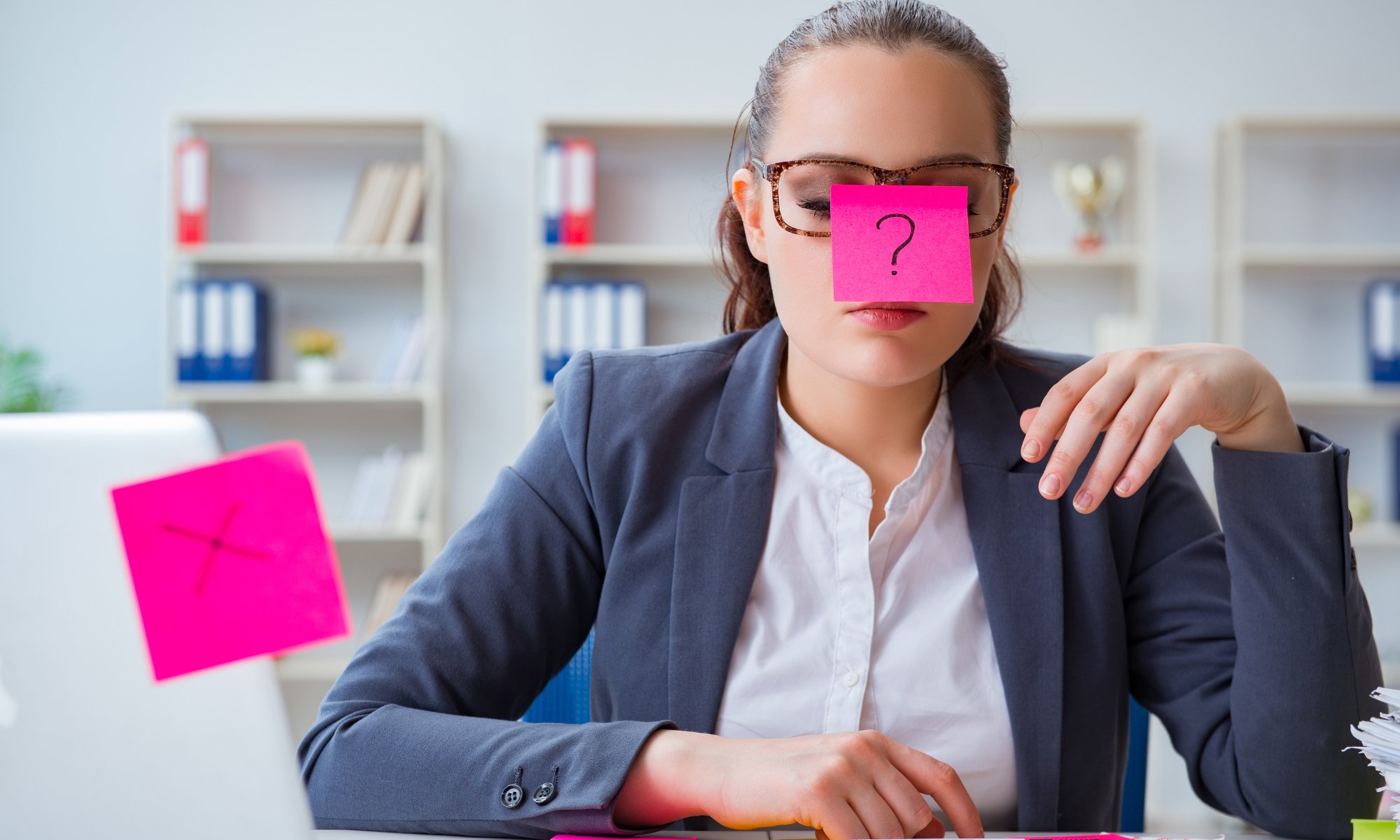 Como se priorizar, se colocar em primeiro lugar. Mulher com expressão confusa, usando óculos e com um post-it rosa colado em sua testa com um ponto de interrogação. Ao lado, um laptop com outro post-it rosa exibindo um "X". A imagem sugere dúvida e indecisão.